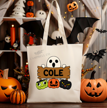 Load image into Gallery viewer, A white canvas tote bag with Halloween-themed decorations, including pumpkins, bats, and ghost images. The bag has area for name personalization. 
