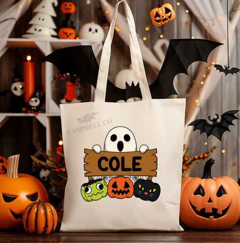 A white canvas tote bag with Halloween-themed decorations, including pumpkins, bats, and ghost images. The bag has area for name personalization. 
